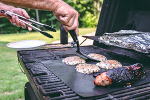 A person grilling chicken using a spatula and tongs on the barbecue.