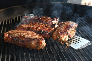 Four chicken pieces cooking on a barbecue grill being flipped with a spatula.