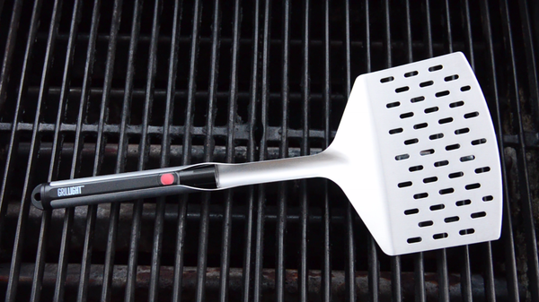 A Giant Edition Grillight LED Spatula laid on top of a grill 
